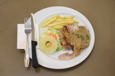 Izgara tavuk ve domuz pastırması kara biber sosu, havuç, ananas ve patates kızartması ile beyaz plaka üzerinde bıçak ve çatal - gıda kavramı ile hizmet.