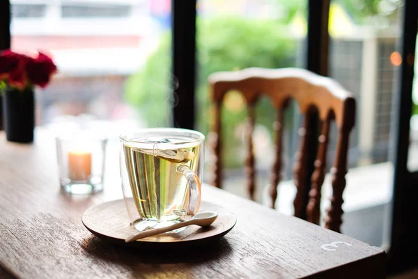 In coffee shop, the hot lavender tea in glass serve with wooden spoon & saucer on the table with chair for relax and slow life concept.