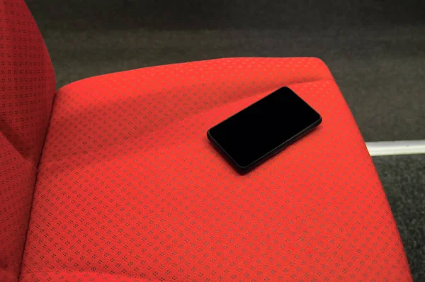 Забутий смартфон з порожнім чорним екраном на червоному стільці високошвидкісного поїзда. Концепція подорожей і загублених гаджетів — стокове фото