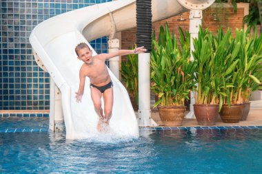 Çocuk (10 yıl) su kaydırağı biniyor. Çocuk ganimet ve eğlenceli havuzda sahip. Risk, güvenlik kurallarının ihlali.