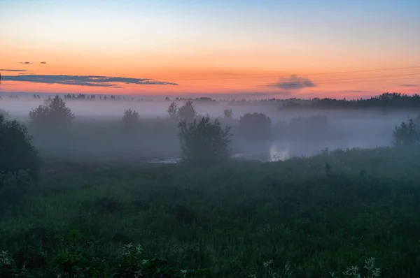 Niebla espesa nocturna sobre el campo y el bosque. Paisaje del cielo nocturno con niebla, cielo naranja y azul . — Foto de Stock