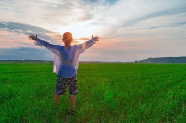 Çocuk kollarını güneş zemin karşı yeşil alanın üzerine yayıldı. Arkadan görünüm. Ellerini yükselterek bir çocukla manzara.