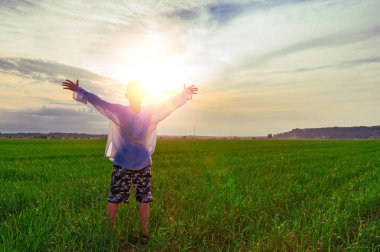 Çocuk kollarını güneş zemin karşı futbol sahası üzerinde yayılmış. Arkadan görünüm. Ellerini yükselterek bir çocukla manzara.