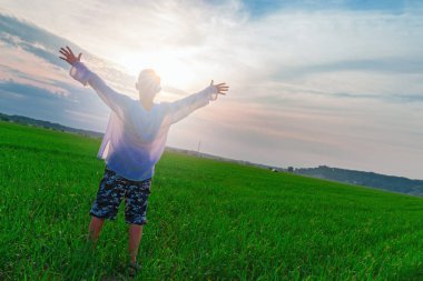 Çocuk kollarını güneş zemin karşı yeşil futbol alan arka plan üzerinde yayılmış. Güzel gün batımı. Arkadan görünüm.