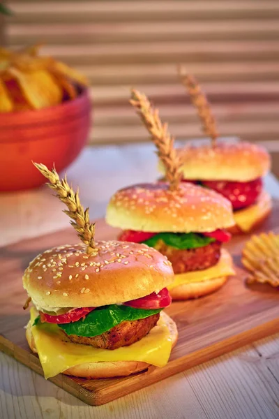 Fila de tres hamburguesas deliciosas de moda en tablero de madera en el restaurante. Enfoque selectivo, perspectiva. Tentadora comida rápida — Foto de Stock