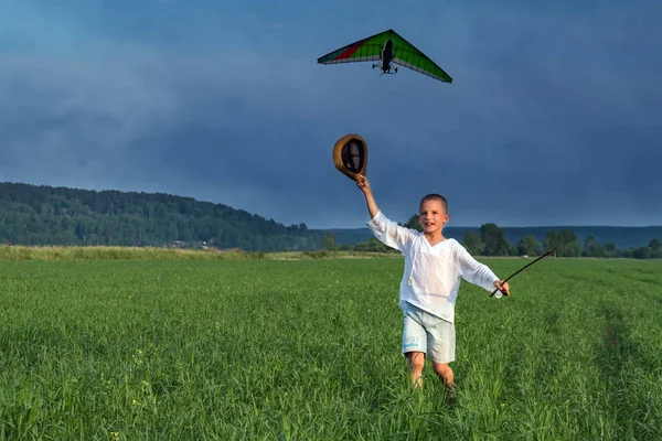 Chłopiec na zielone pole macha kapelusz latające skrzydło. Macha kapelusz chłopiec. — Zdjęcie stockowe