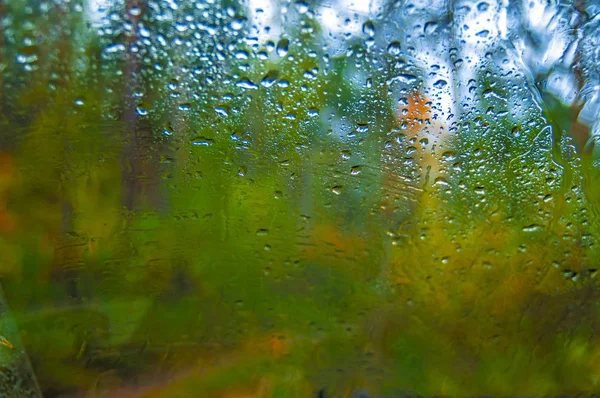 Agua gotas azules de lluvia en la ventana. Desenfoque bosque de otoño en el fondo. Otoño lluvioso oscuro paisaje . — Foto de Stock