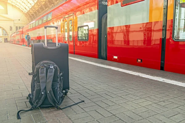 Mochila y maleta en la estación de tren con un viajero. Puesta del sol, concepto de viaje . — Foto de Stock