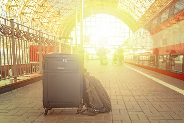 Mochila y maleta con ruedas en la estación de tren a la luz del sol. Concepto de viaje . — Foto de Stock