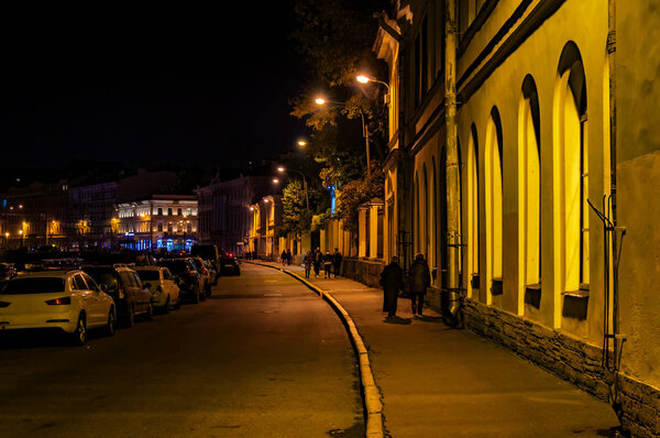 Night street in the old part of the European city. The yellow light from the street lamps on the low-rise buildings and the sidewalk