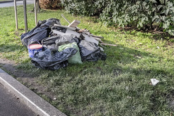 Gran cantidad de residuos de construcción en el césped en el Parque. Bolsas de basura negras y tablas sobre hierba verde. Desperdicios del territorio , — Foto de Stock