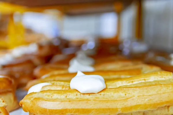 Klassisk konditor i bakeriet. Tradisjonelle Eclair-pundkaker med kondensert melk og vaniljesaus. Lage kaker, profitroller, eclairfransk, selektivt fokus – stockfoto