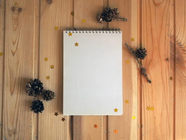 Mock up notepad. Open notebook empty blank page on wooden background with fir cones and confetti stars. Top view