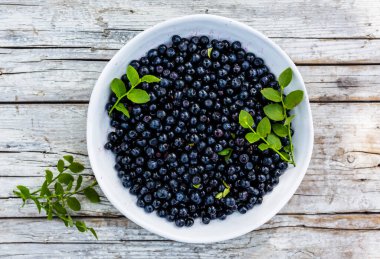 Ahşap arka planda bir kasede taze toplanmış yaban mersini..