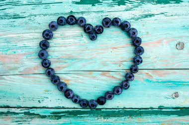 Ahşap bir arka planda kalp şeklinde dizilmiş taze toplanmış yaban mersini..