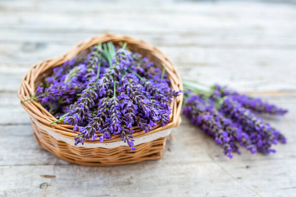 Lavender flowers in a heart-shaped basket on a wooden background.