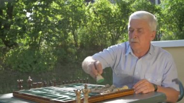 Yaşlı gri saçlı adam bahçede satranç oyununu hazırlıyor ve beyaz figürleri yan yana koyuyor..