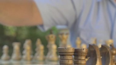 Ön manzara. Yaşlı adam bahçedeki masada satranç oyununu hazırlıyor ve siyah figürleri tahtaya yerleştiriyor..