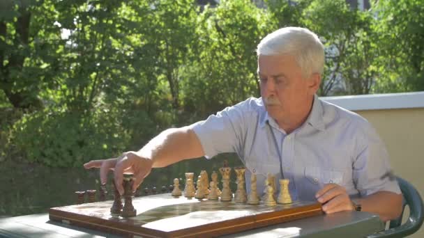 Γέρος Γκριζομάλλης Προετοιμάζει Παιχνίδι Σκακιού Έξω Στον Κήπο Στο Τραπέζι — Αρχείο Βίντεο