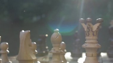 Masadaki tahta satranç oyunu bir kamera içinde soldan sağa, güneş ışığına doğru mercekle kayıyor.