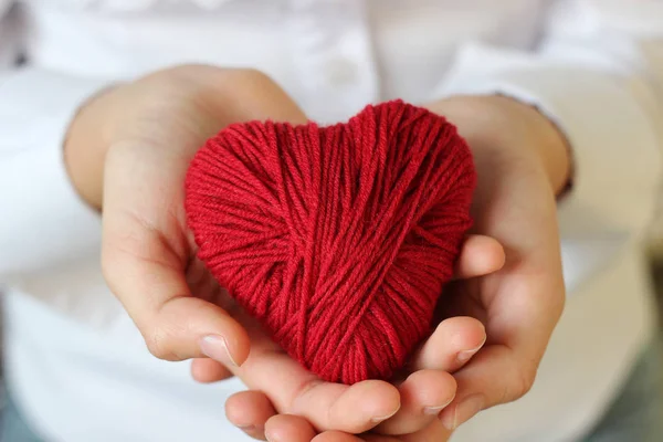 Le mani da bambini tengono un cuore di filo rosso per lavorare a maglia . — Foto Stock