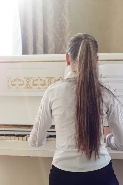 Girl playing on white piano. A view from the back of the girl si — Stock Photo, Image