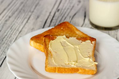 Ahşap bir tahta üzerinde beyaz bir tabak ekmek ve tereyağı ile hala hayat