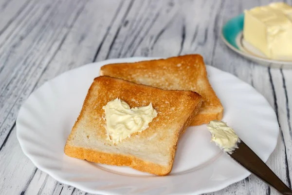 Ahşap bir tahta üzerinde beyaz bir tabak ekmek ve tereyağı ile hala hayat