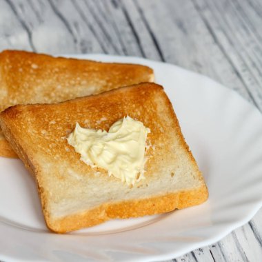 Ahşap bir tahta üzerinde beyaz bir tabak ekmek ve tereyağı ile hala hayat