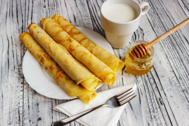 Bal ve bir fincan süt ile beyaz bir tabak üzerinde krep. Ahşap b