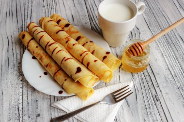 Bal ve bir fincan süt ile beyaz bir tabak üzerinde krep. Ahşap b