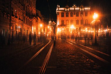 Old European illuminated city at rainy night. People walking on the night street clipart