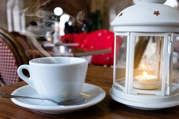Una taza de café caliente cerca de una linterna con una vela sobre el interior de la cafetería — Foto de Stock