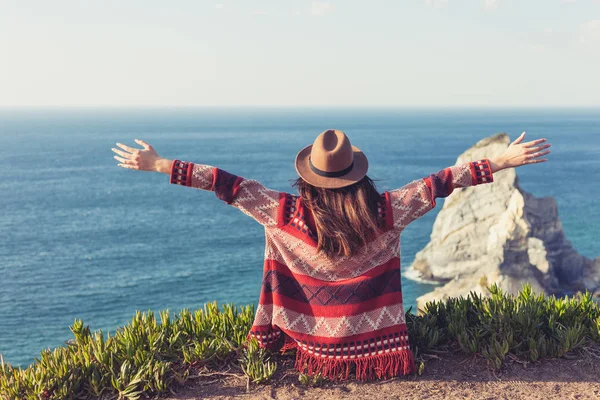 Primer plano vista trasera de la mujer en ropa de viaje y sombrero sentado y mirando el océano azul y el cielo . — Foto de Stock