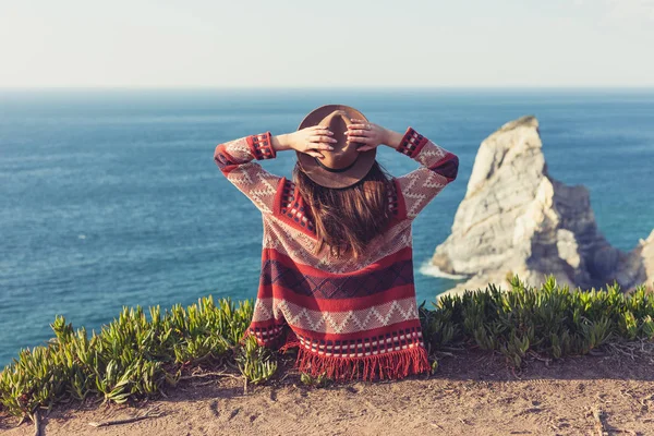 旅着や帽子をかぶった女性のクローズアップバックビューは、青い海と空を見て座って. — ストック写真