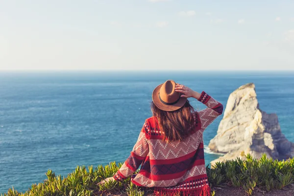 Primer plano vista trasera de la mujer en ropa de viaje y sombrero sentado y mirando el océano azul y el cielo . — Foto de Stock