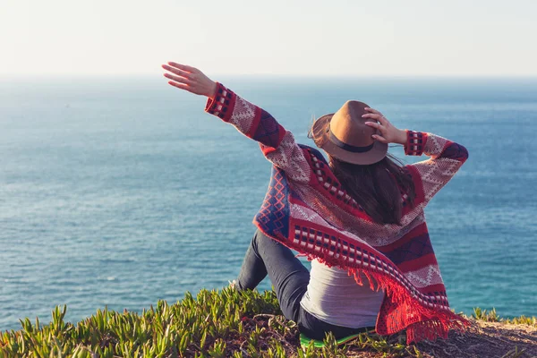 Nahaufnahme Rückansicht einer Frau in Reisekleidung und Hut, die sitzt und auf blauen Ozean und Himmel blickt. — Stockfoto