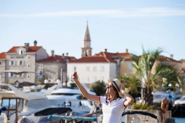 Fiatal utazó nő kalapban fotózni selfie nyári napos mediterrán város kamera okostelefon. Barna lány így fotográfia nyaralás — Stock Fotó