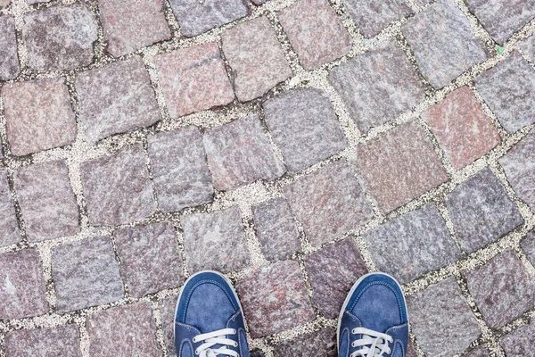 Man feet in blue jeans sneakers on cobbled road — Stock Photo, Image