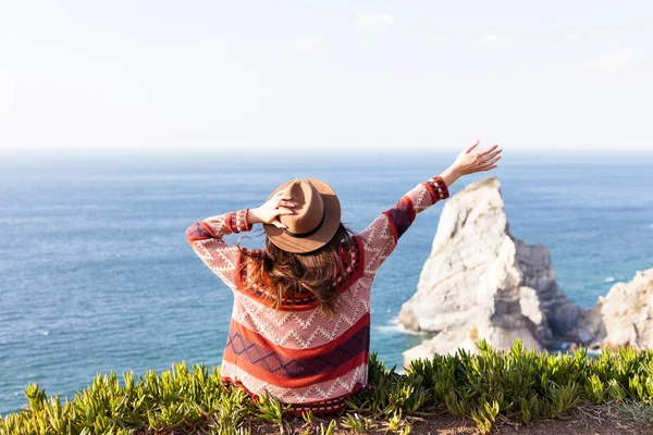 Primer plano vista trasera de la mujer en ropa de viaje y sombrero sentado y mirando el océano azul y el cielo . — Foto de Stock