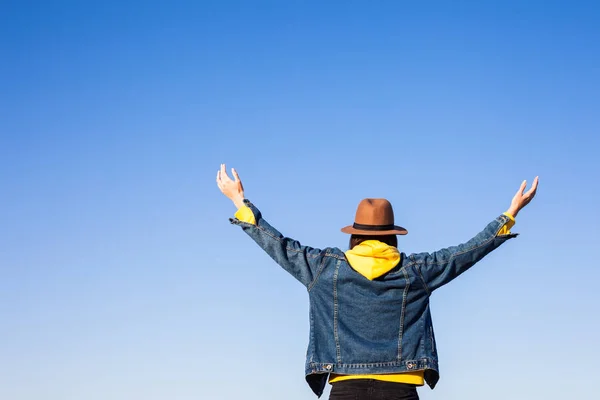 Primer plano vista trasera de la mujer en ropa de viaje y sombrero sentado y mirando el océano azul y el cielo . —  Fotos de Stock