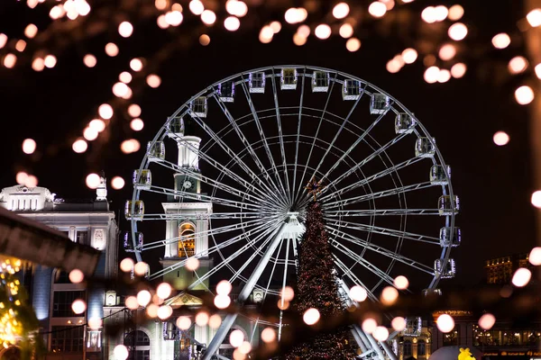 Rueda de la fortuna en el mercado de Navidad. Fuera de foco, las luces de la ciudad nocturna. Feria de Navidad — Foto de Stock