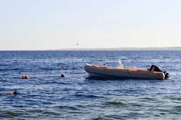 An inflatable gray boat, a motor boat with a motor on the salt blue sea against the background of buoys and distant mountains.