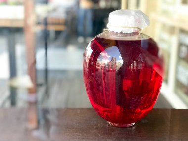 Kırmızı büyük cam üç-litre banka bir istif, suyu, iksir bulanık bir arka plan üzerinde ahşap kapaklı.