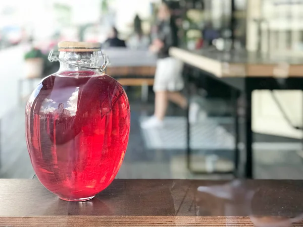 Büyük güzel üç litrelik cam banka bir jambon, suyu, iksir, parlayan bir sıvı bulanık bir arka planda bir kafede bir raf ahşap kapaklı bir içkiyle.