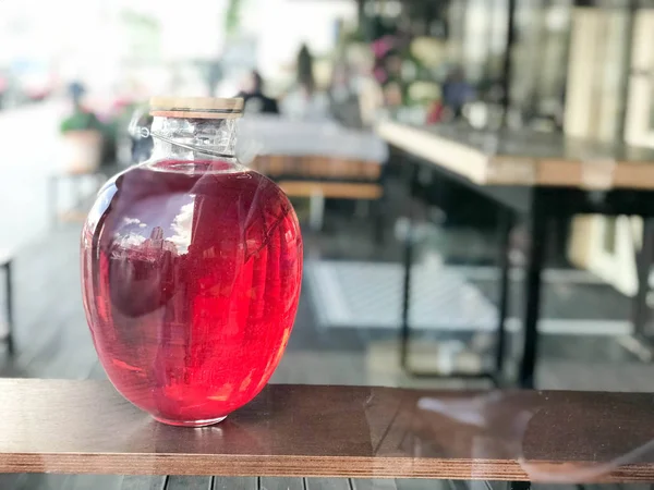 Büyük bir cam üç-litre olabilir campote, suyu, iksir bulanık bir arka planda bir raf ahşap kapaklı parlayan bir sıvı ile.