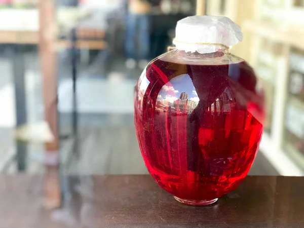 Kırmızı büyük cam üç-litre banka bir istif, suyu, iksir bulanık bir arka plan üzerinde ahşap kapaklı.