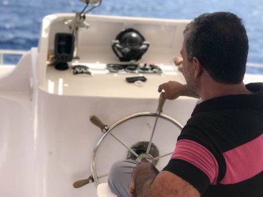 Yağız bir Kaptan, kırmızı çizgili gömlekli, bir Arap adam bir gemi, denizde dümene oturan bir tekne yönetir.