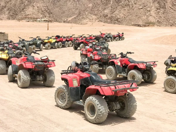 The big turn is a lot of four-wheeled multi-colored powerful fast off-road all-wheel drive ATVs, motorcycles in the sandy hot desert in the parking lot against the backdrop of high mountains.