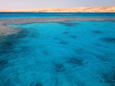 Açık mavi doğal deniz tuzlu su, deniz, okyanus dalgaları ile bir alt güzel mercan resifleri ile peyzaj taşlar sarı arka planı taş uzak dağlar.